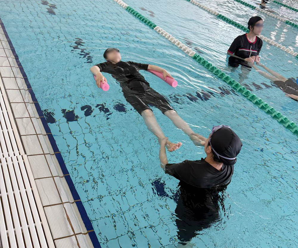助産師さんに足をサポートされながら、プールで全身の力を抜き、両腕の浮きを持ちながら水面に浮く妊婦さん