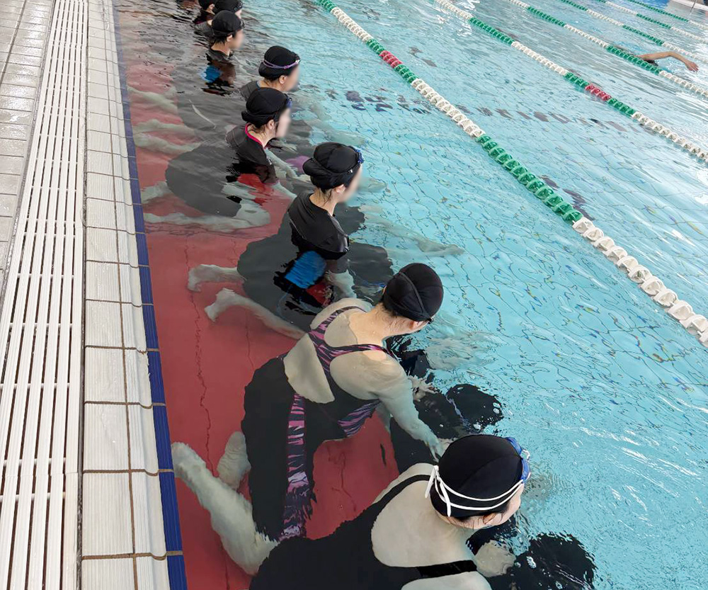 プールのレーンの端の水中で水着を着た妊婦さんが水中座禅をしている